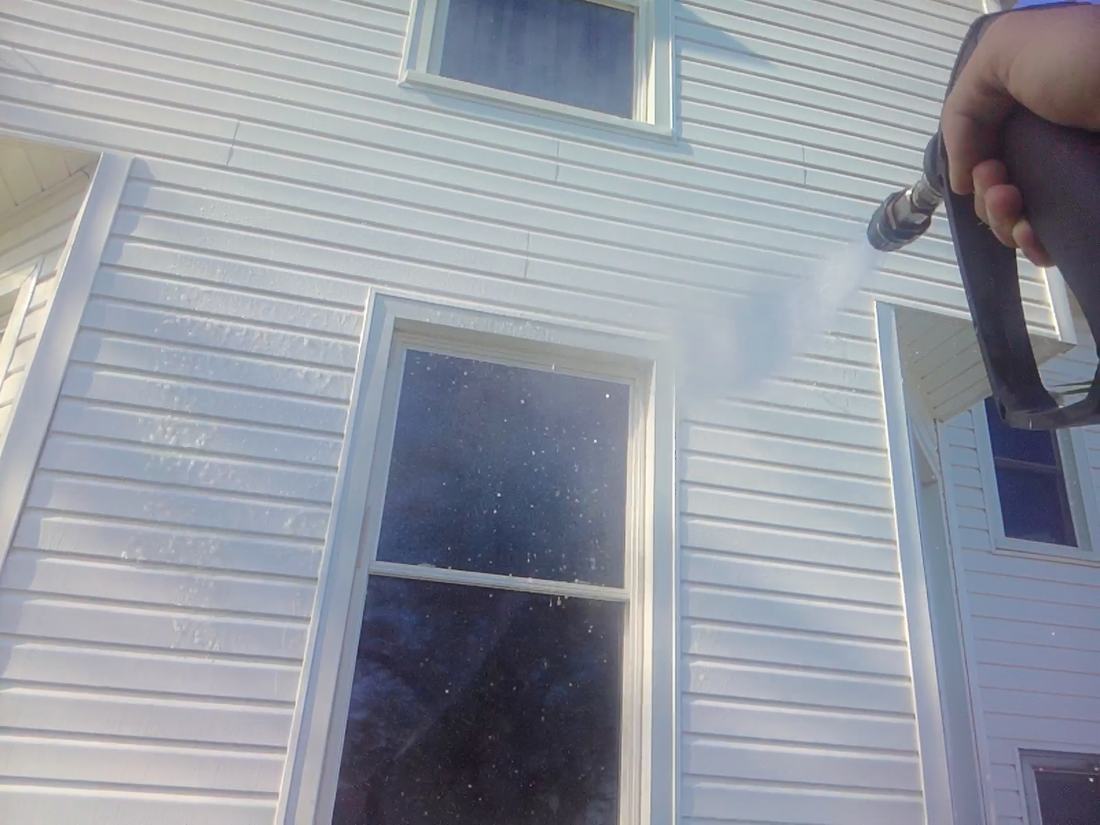 Soft washing around a window and its trim on white vinyl siding